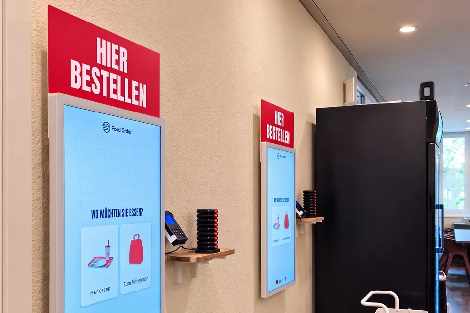 Zwei Bestellterminals mit «Hier bestellen»-Schild, Kartenterminal und Pagern an der Wand (Symbolbild auf Basis einer Aufnahme des Lokals)